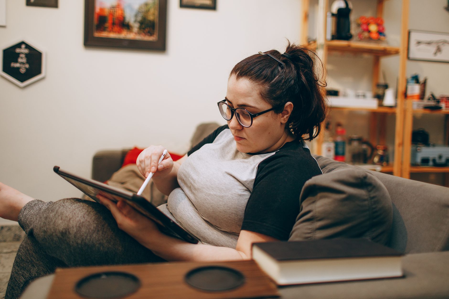 Une femme portant des lunettes, installée sur un canapé, qui consulte une tablette.