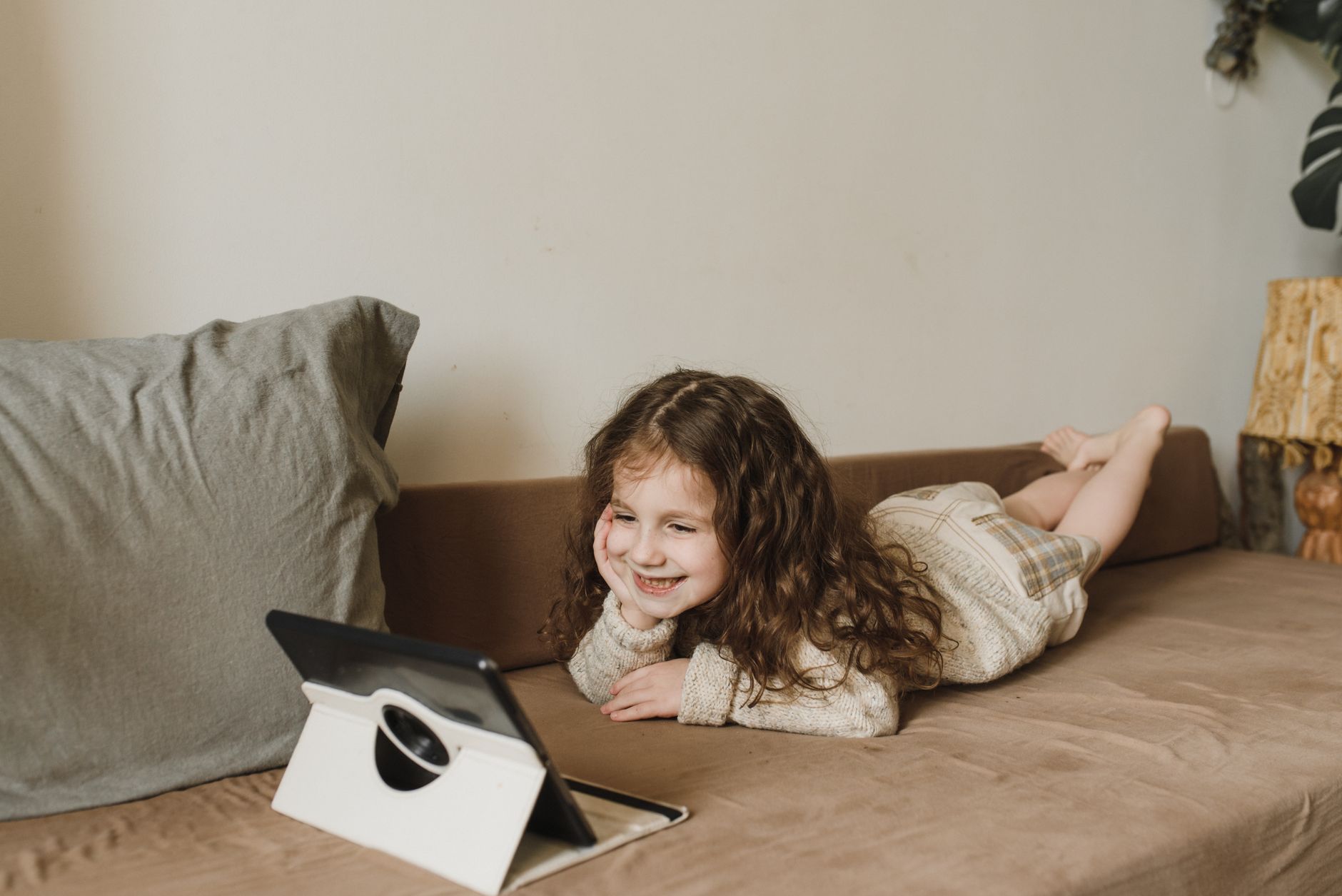 Une jeune fille allongée sur un canapé, en train de regarder une tablette avec le sourire.