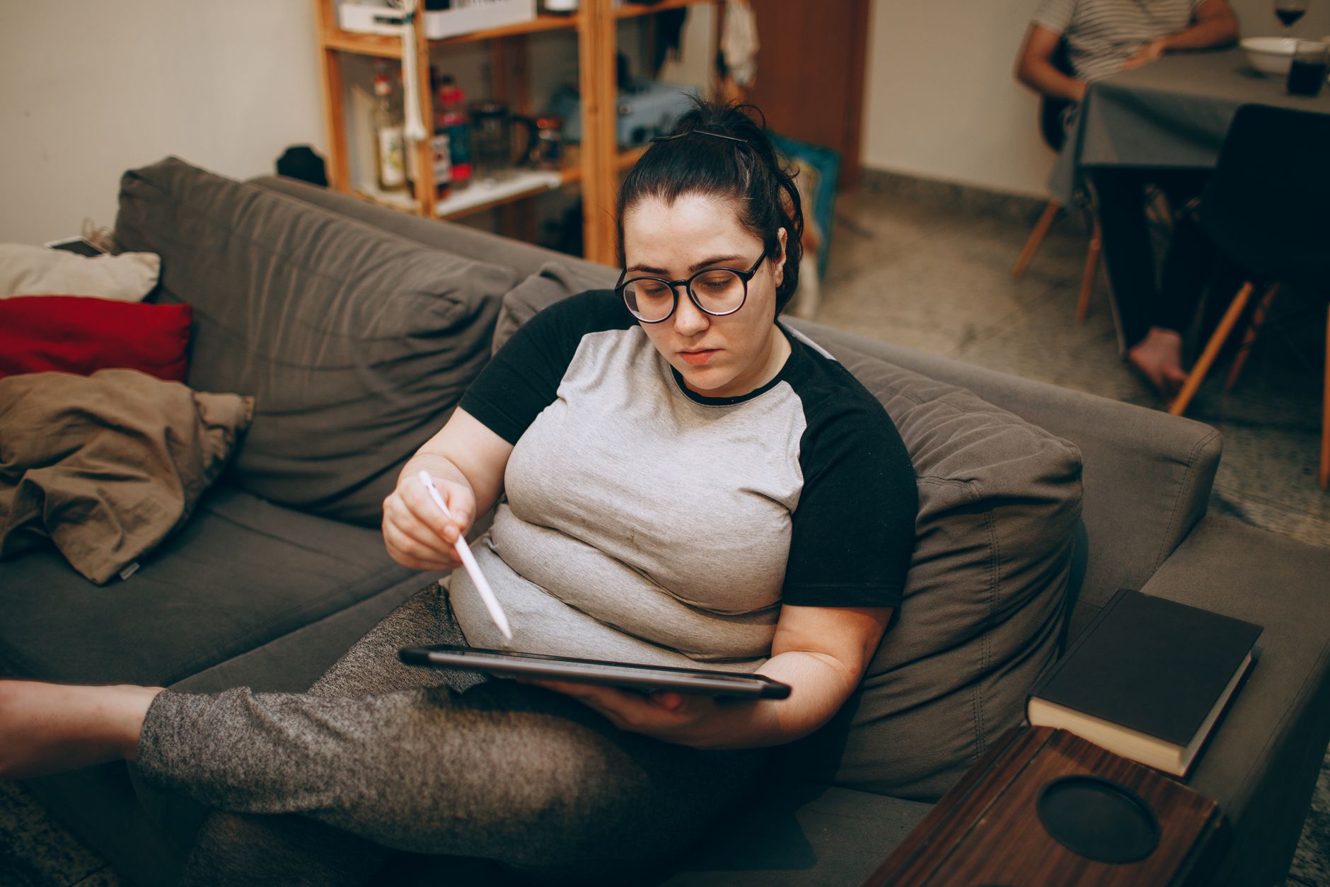 Une femme assise sur un canapé, stylet numérique en main, en train de travailler sur une tablette.
